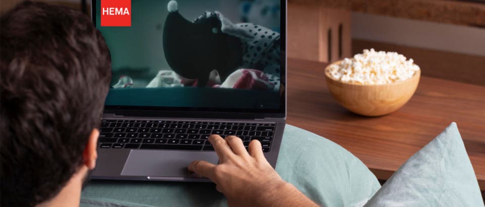 A person watching something on his laptop with popcorn on the sidetable.